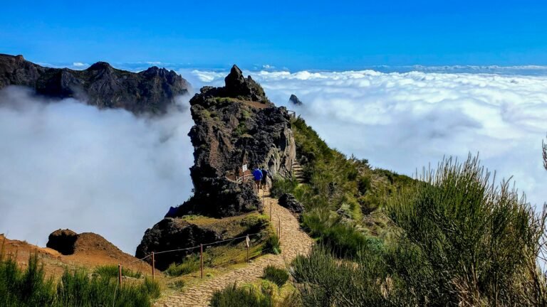 Hikers on a mountain trail at Pico do Arieiro in Madeira above a thick layer of white clouds.