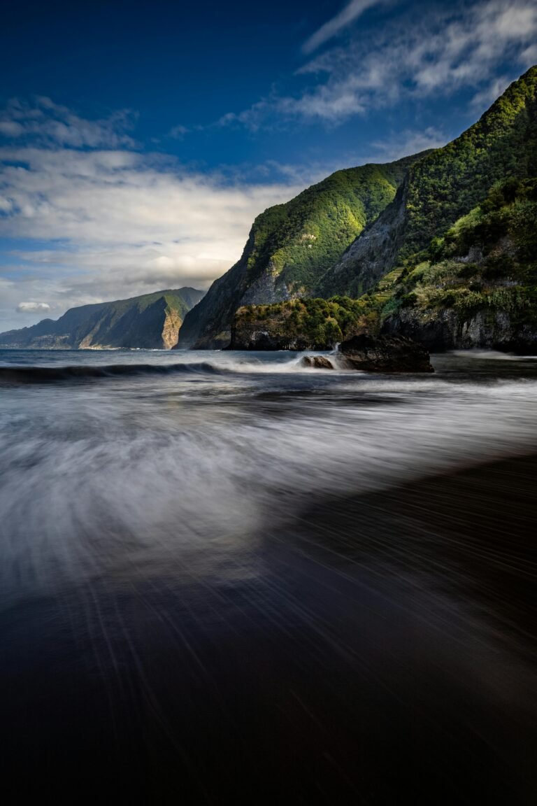 Black sand beach with lush green mountains and cliffs in Madeira.