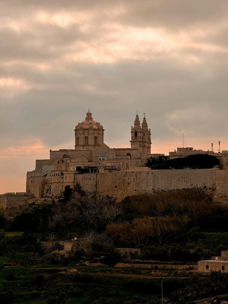 Panoramic view of the historic Mdina Cathedral and fortified city walls in Malta at sunset.